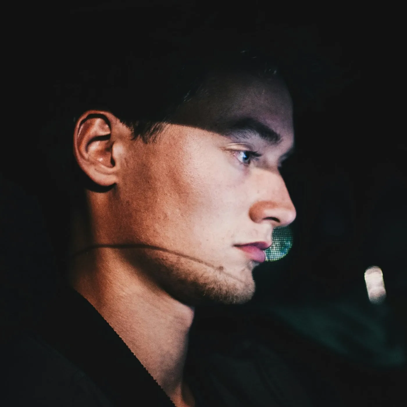 Young man in profile, his face lit by the soft glow of a screen in a dark room