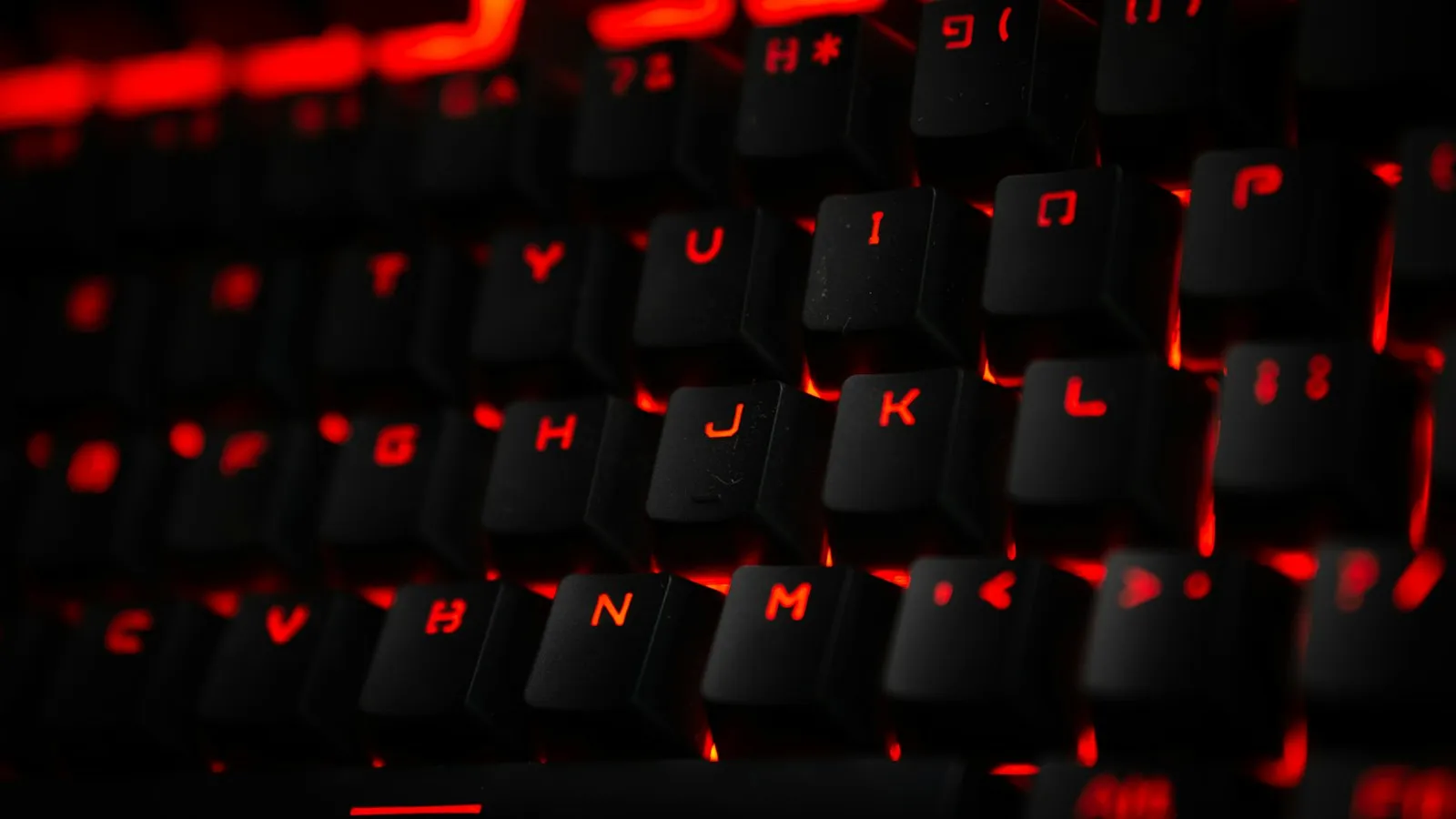 Close-up of a black mechanical keyboard with glowing red backlit keys in a dark room
