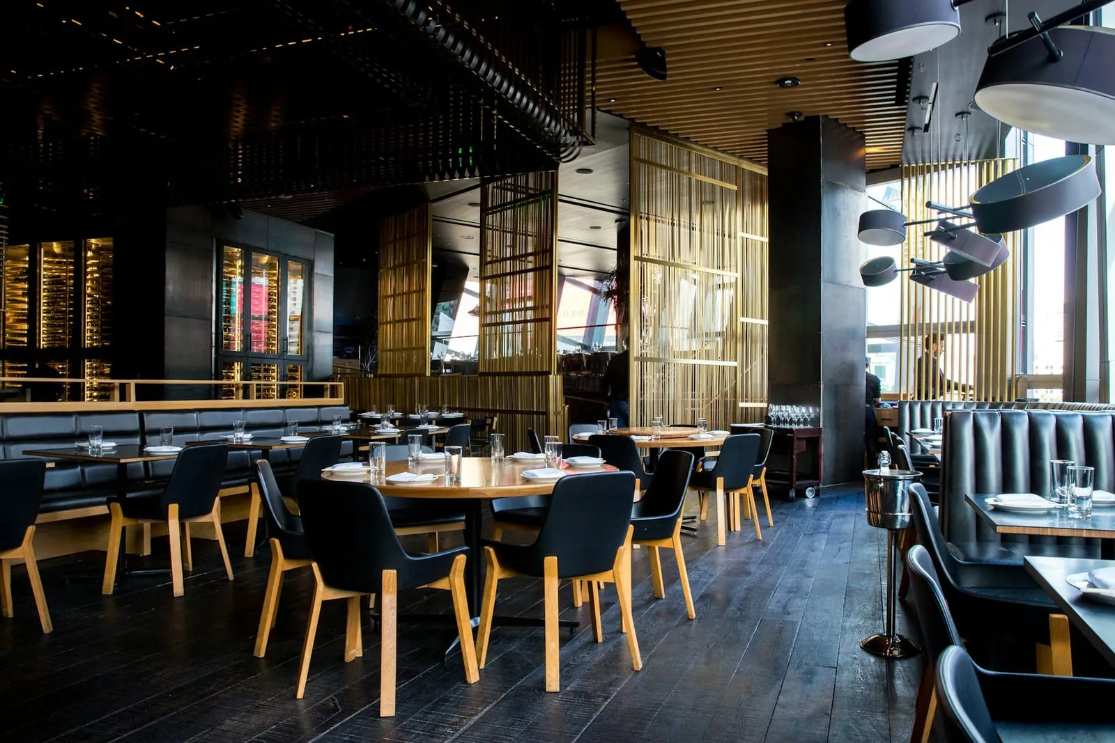 Interior of an upscale restaurant with warm lighting, wooden tables and a long bar