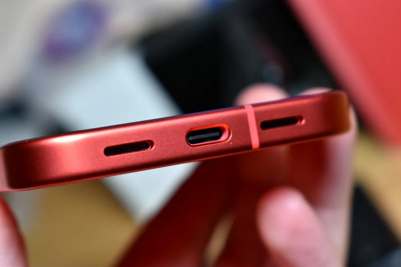 Close-up of a red smartphone held in hand, showing its USB-C port and speaker grilles
