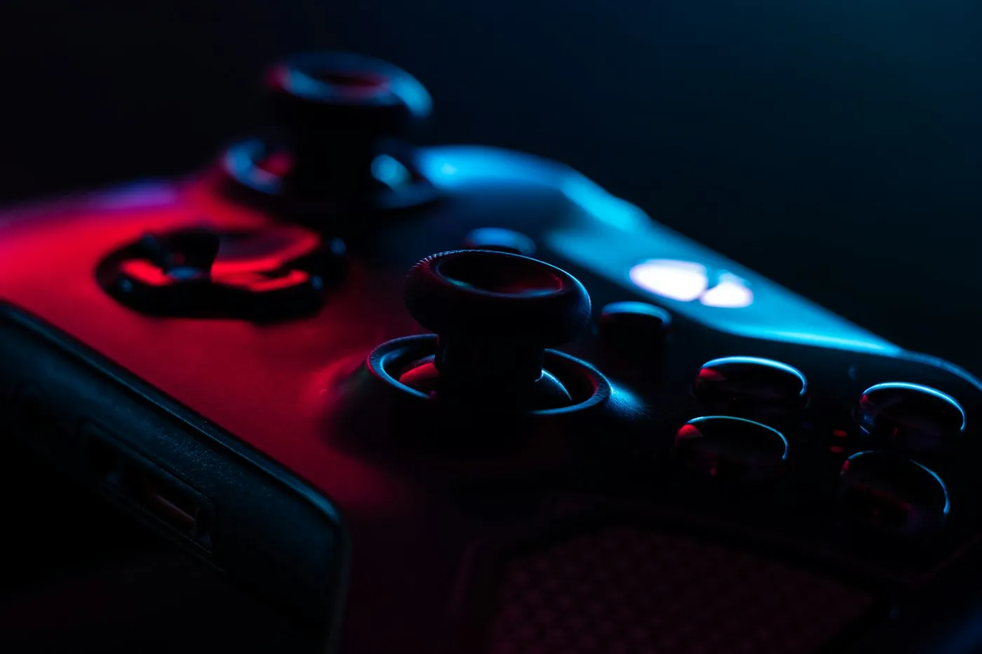 Close-up of a black game controller's thumbsticks and face buttons in red and blue light