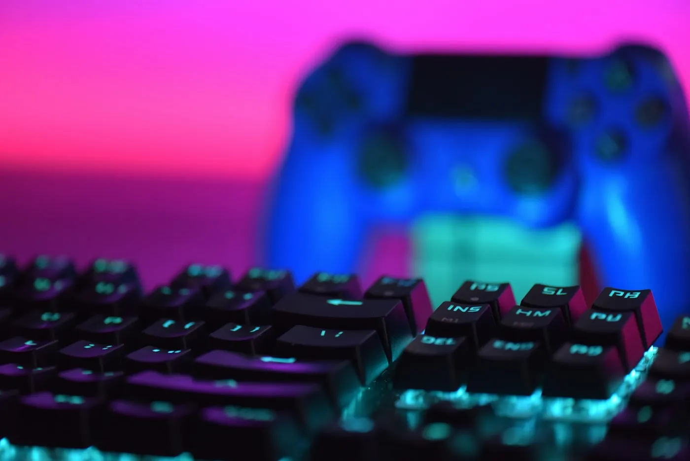 Backlit mechanical keyboard in front of a blurred game controller under pink and blue light