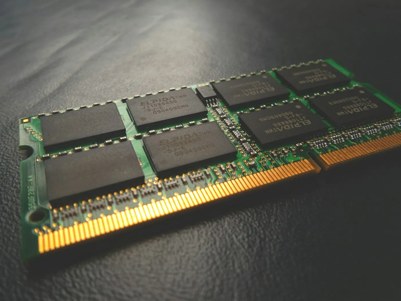 Close-up of a laptop SO-DIMM memory module with gold contacts on a dark textured surface