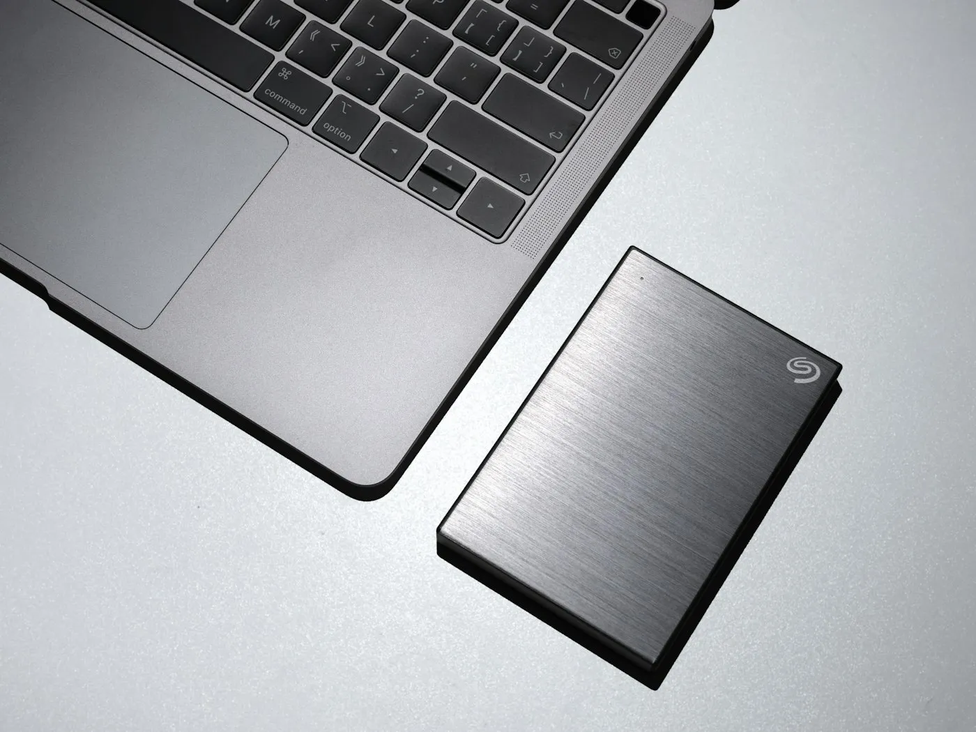 A slim silver portable external hard drive lying beside an open laptop keyboard