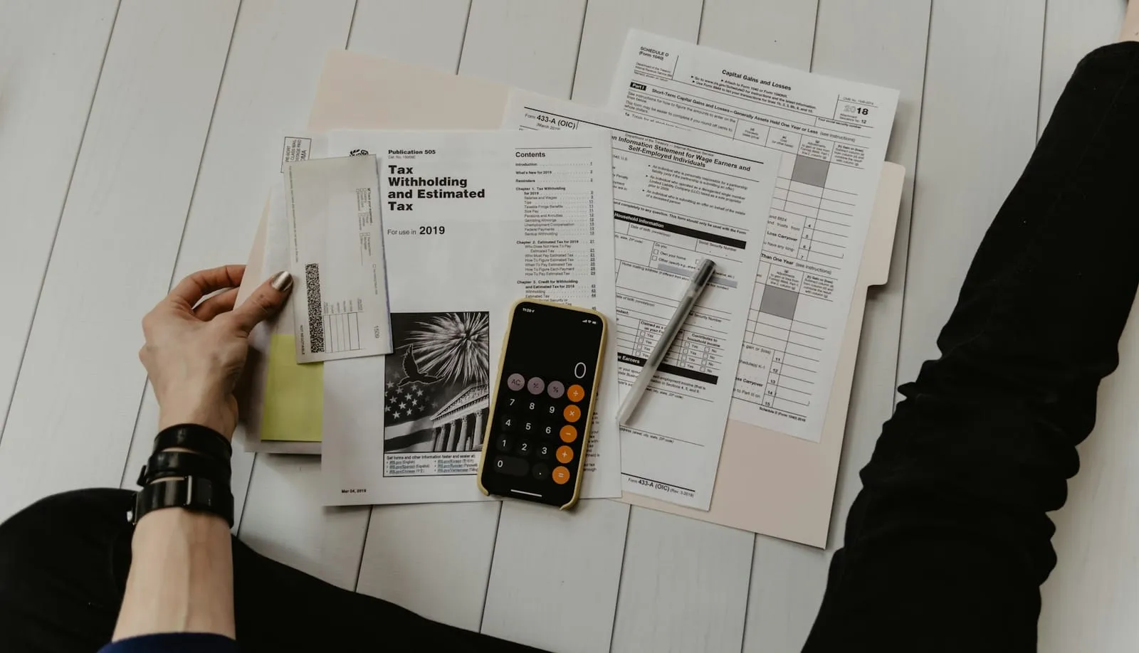 Hands holding tax and financial forms on a white table next to a calculator and a pen