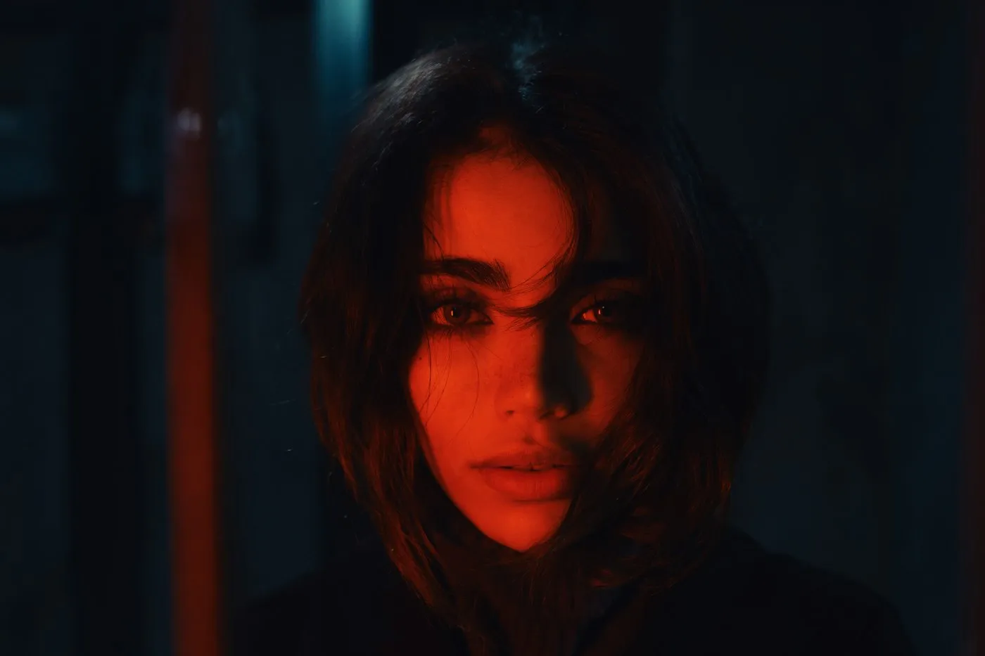 Close-up portrait of a woman's face half-lit by red light against a dark background