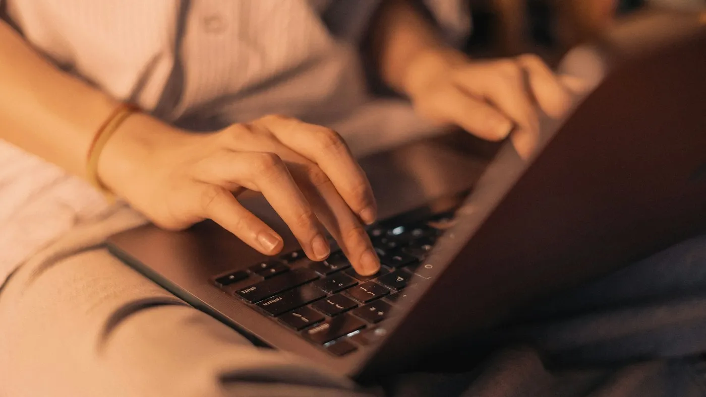 Close-up of hands typing on a laptop keyboard in warm, low evening light
