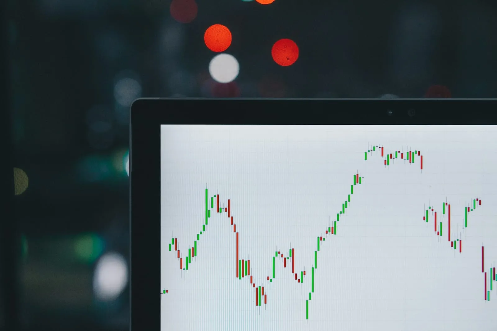 A laptop screen in a dark room showing a rising stock market line chart