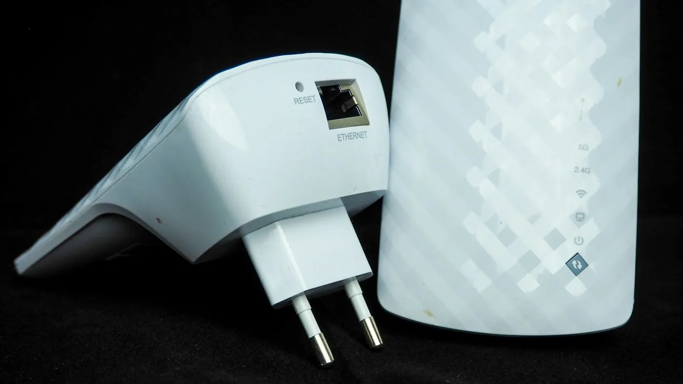 Two white plug-in Wi-Fi range extenders, one showing its plug and Ethernet port, on black