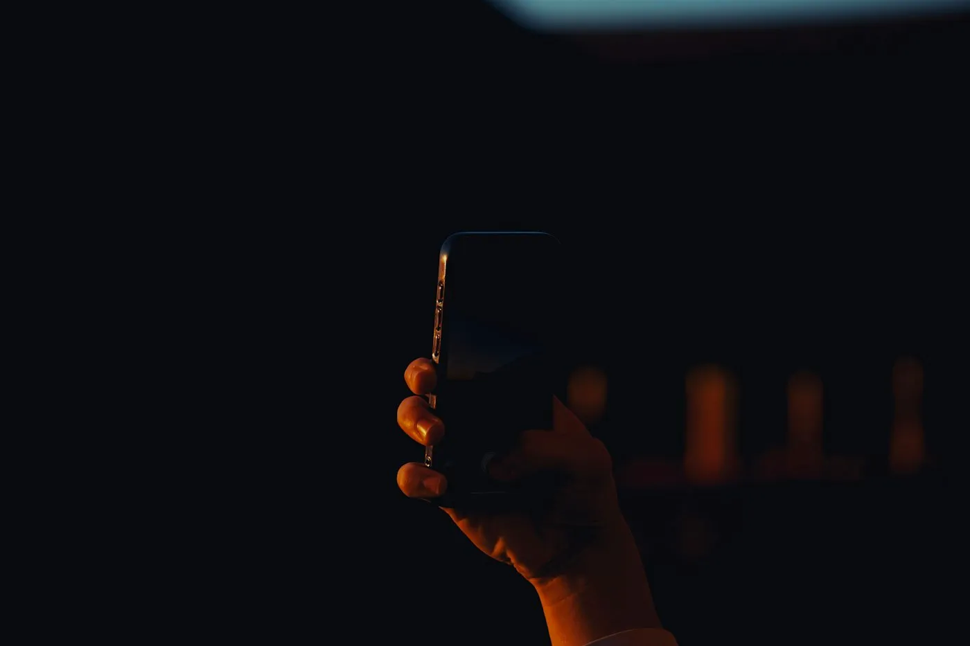 Hand holding a smartphone against a dark background, lit by warm evening light