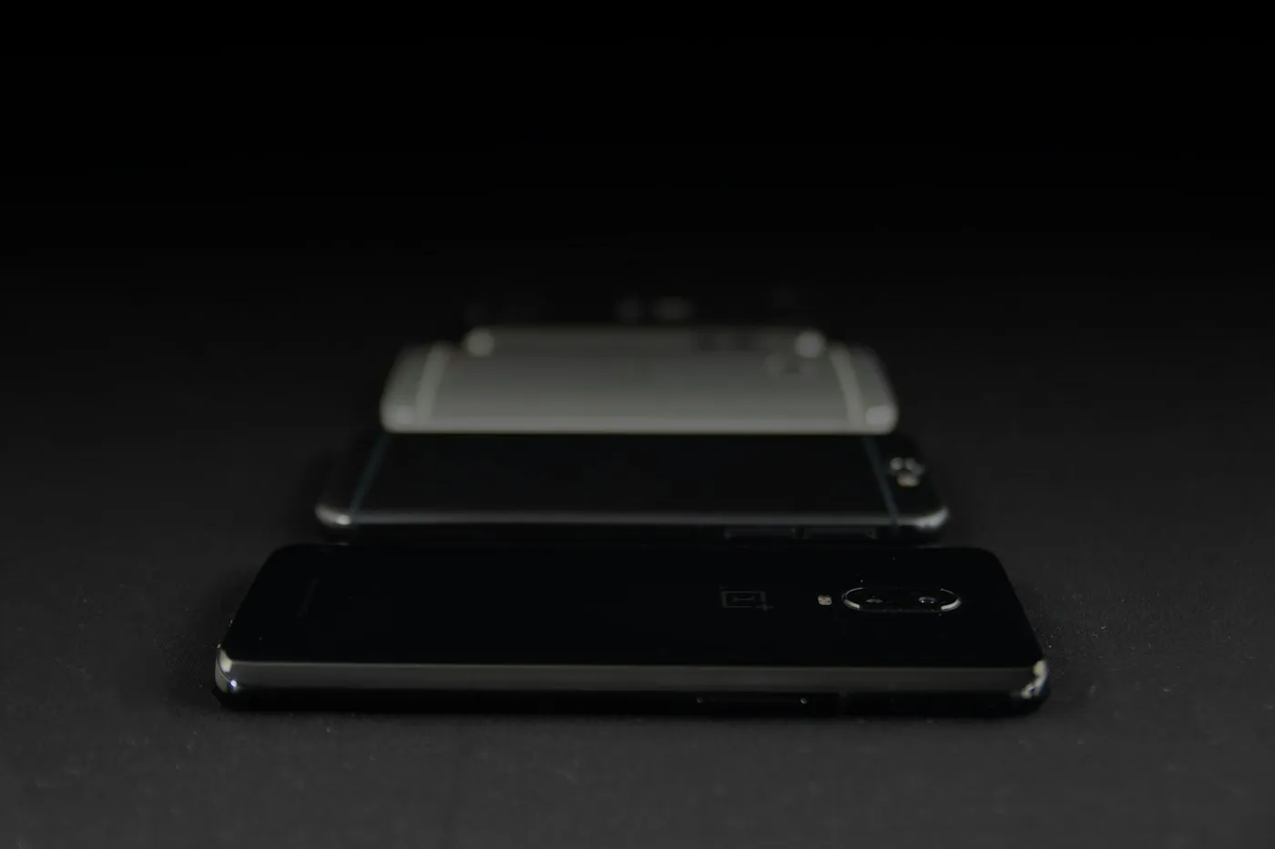 Black OnePlus phone face down on a dark surface, with more blurred phones lined up behind it