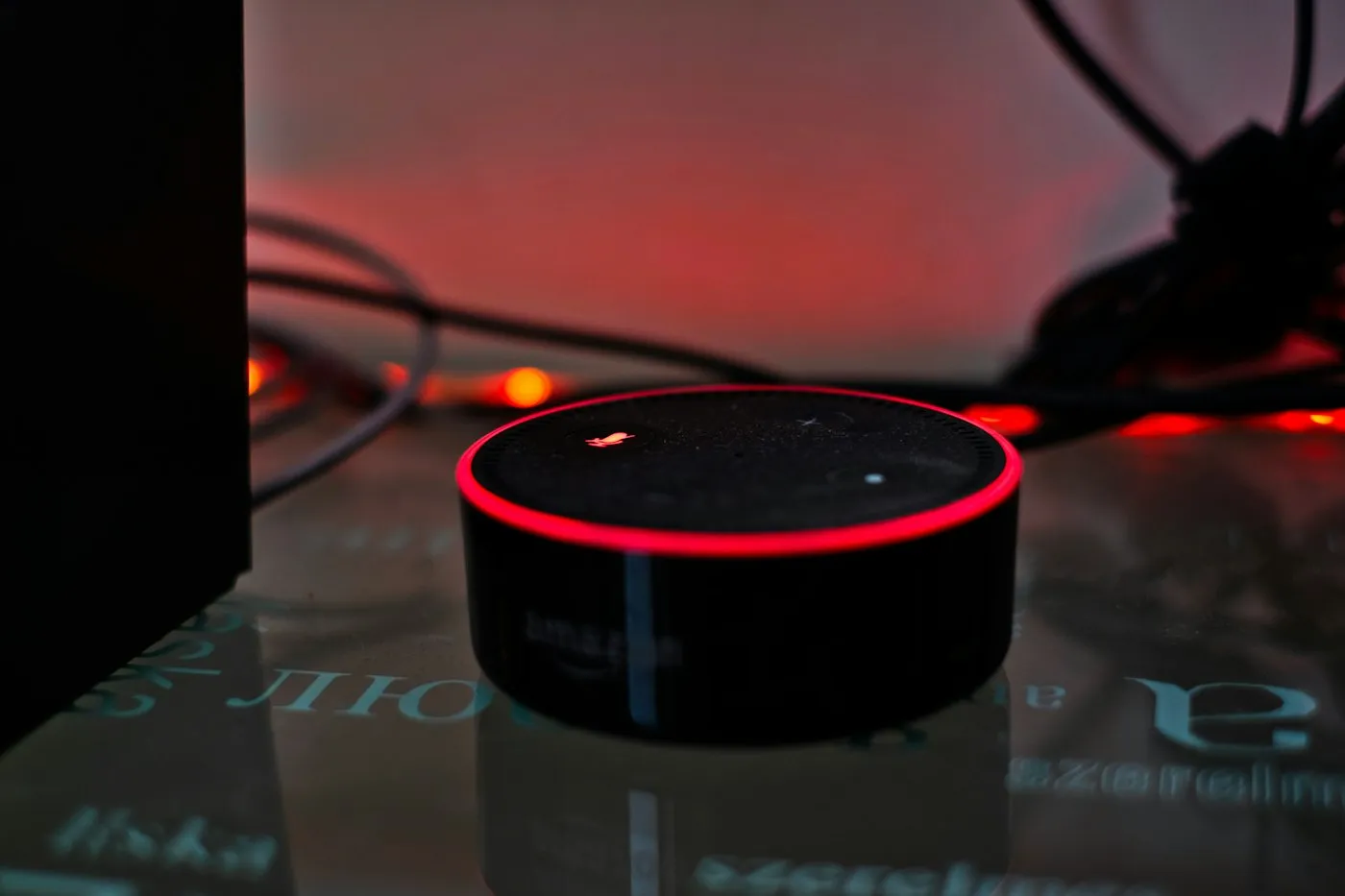 Smart speaker glowing with a red ring, its microphone muted, on a dark glass table