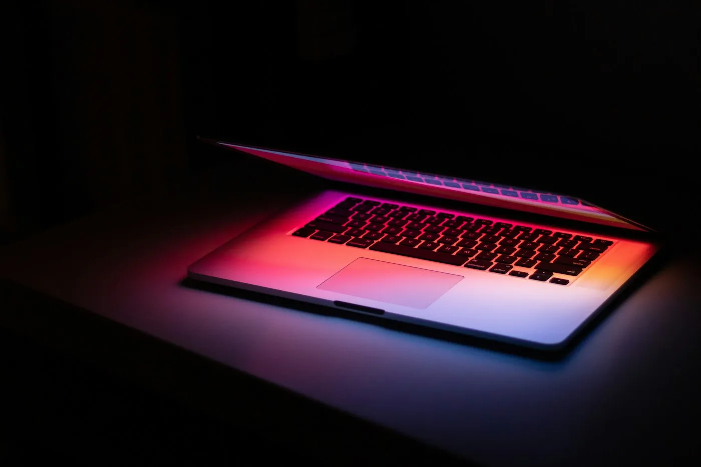 A half-open silver laptop glowing with red and pink light in a dark room