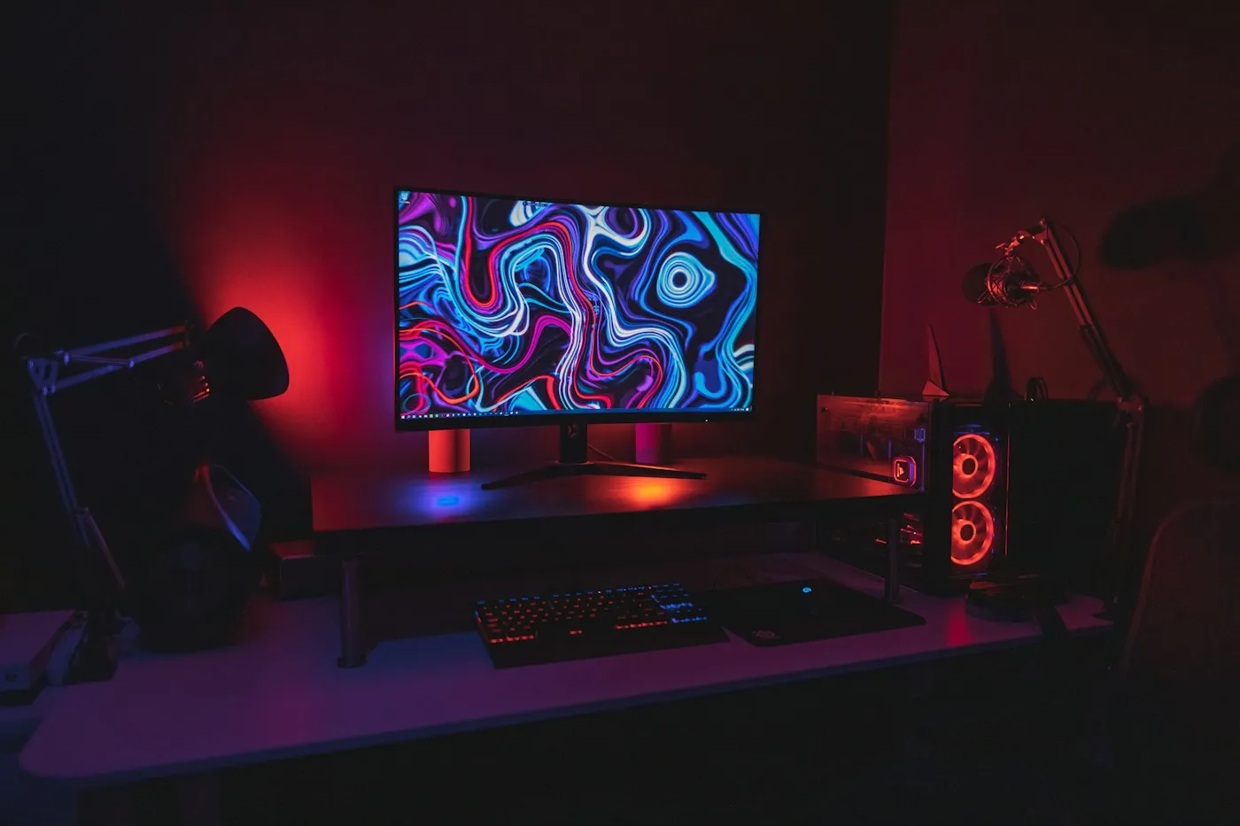 Gaming desk with a glowing monitor, RGB keyboard and red-lit PC tower in a dark room