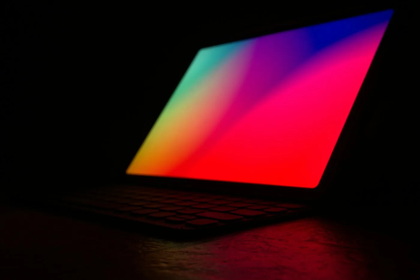 Open laptop glowing with a red and violet gradient screen in a dark room