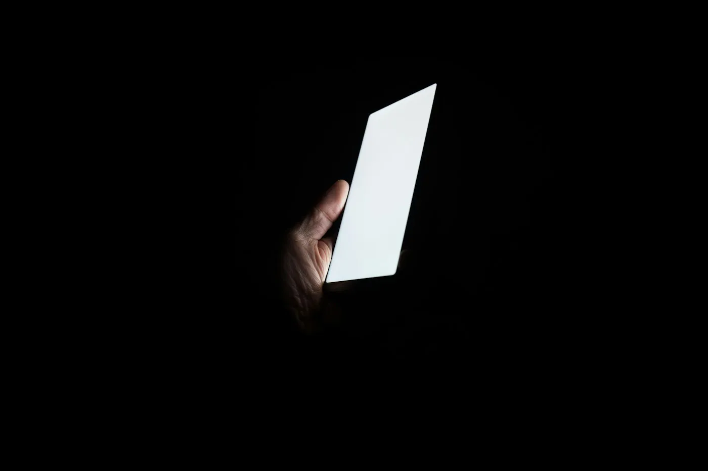 Hand holding a smartphone with a bright white screen against total darkness