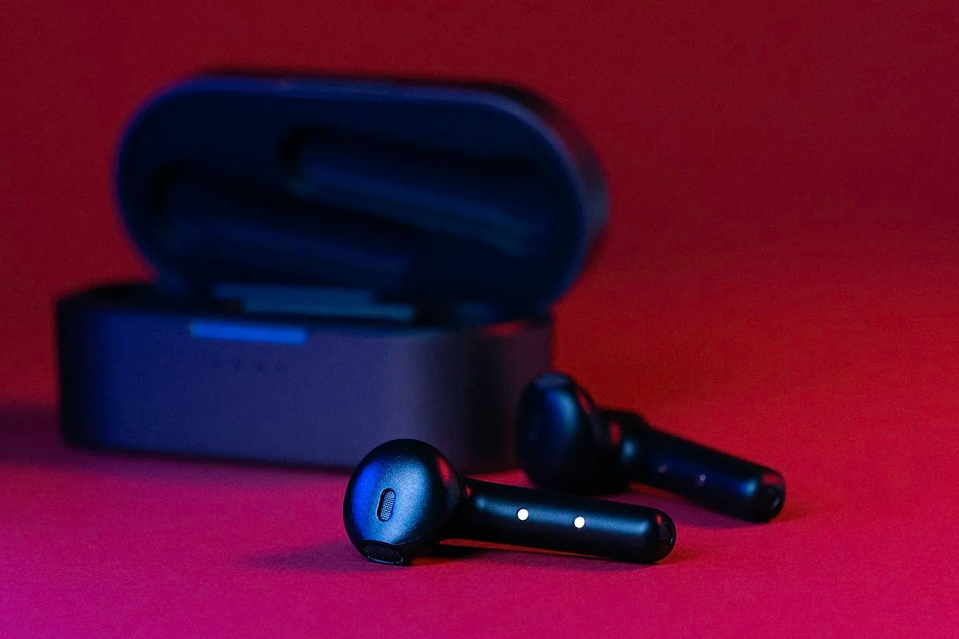 Black wireless earbuds in front of their open charging case under moody red light