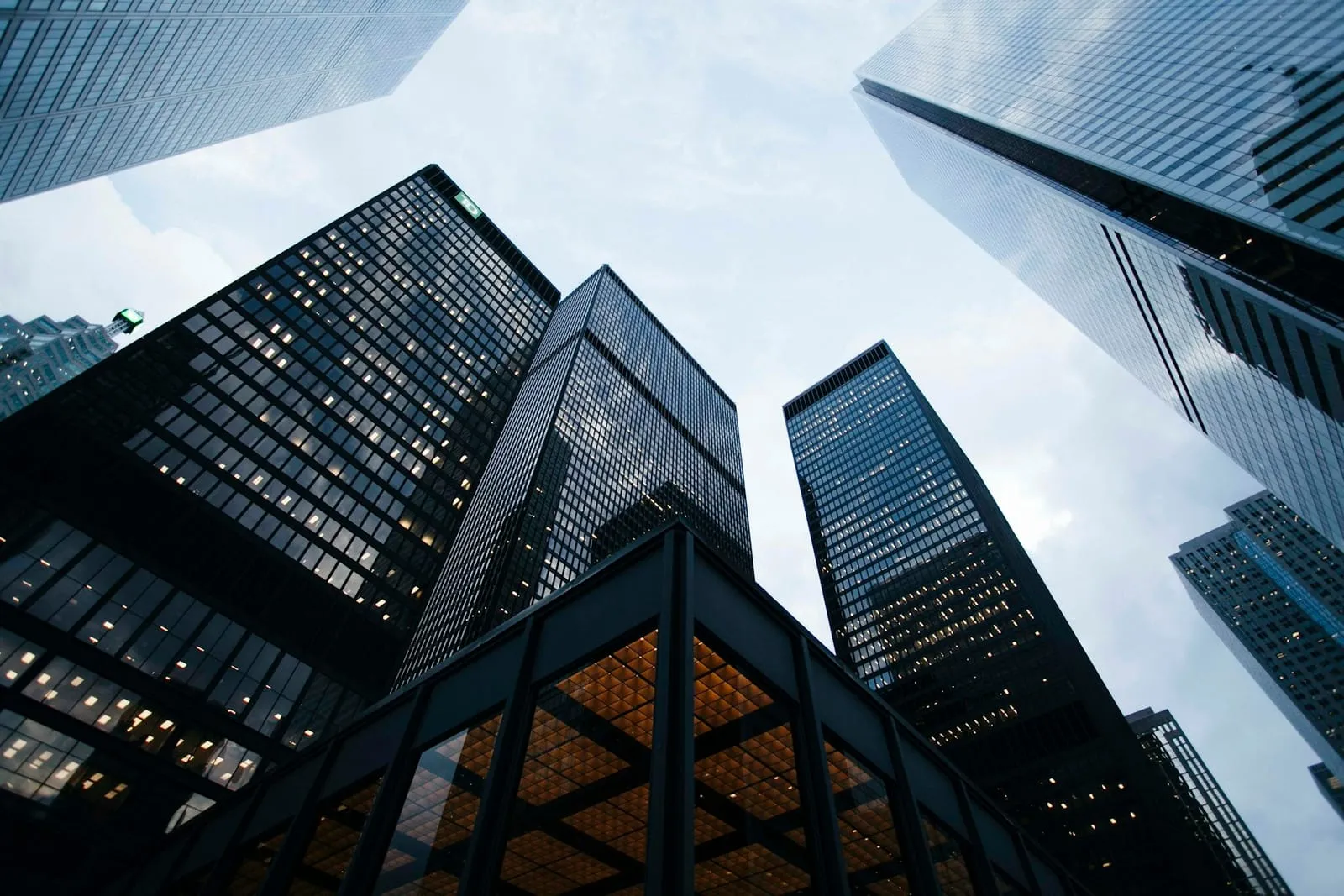 Glass office towers seen from street level, rising into a cloudy sky