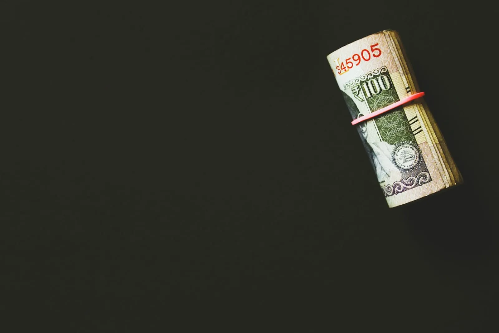 Rolled bundle of US dollar banknotes held by a rubber band on a black surface