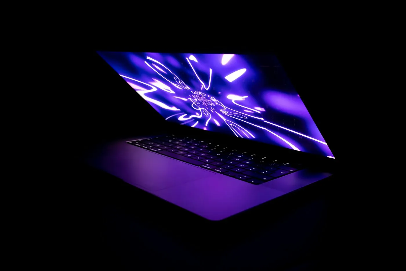 Open laptop with a bright purple light-burst screen glowing in a pitch-dark room