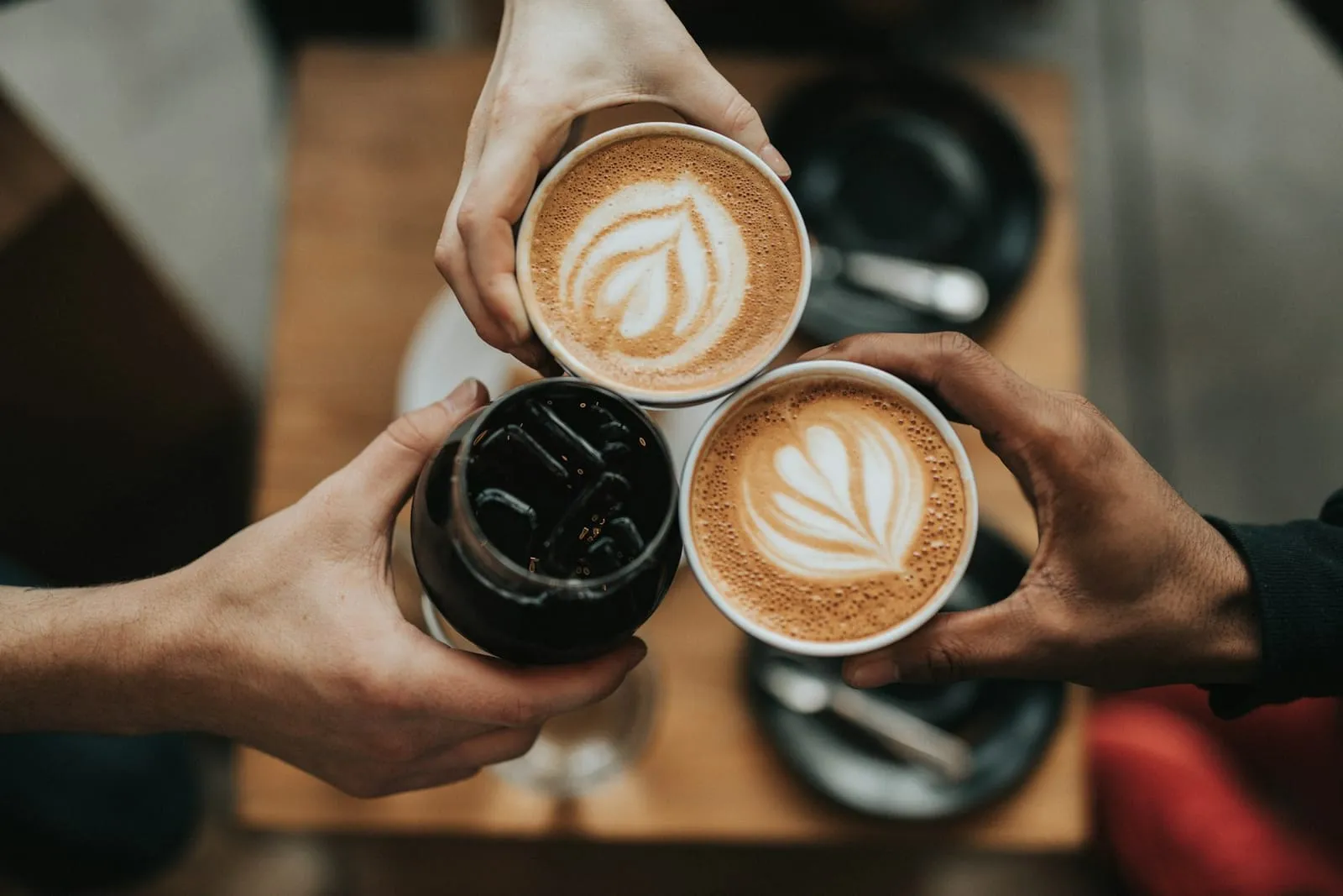 Four hands holding coffee cups with latte art together over a wooden table