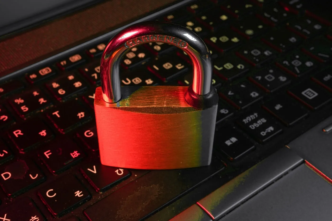 Metal padlock resting on a dark laptop keyboard, lit by dramatic red light