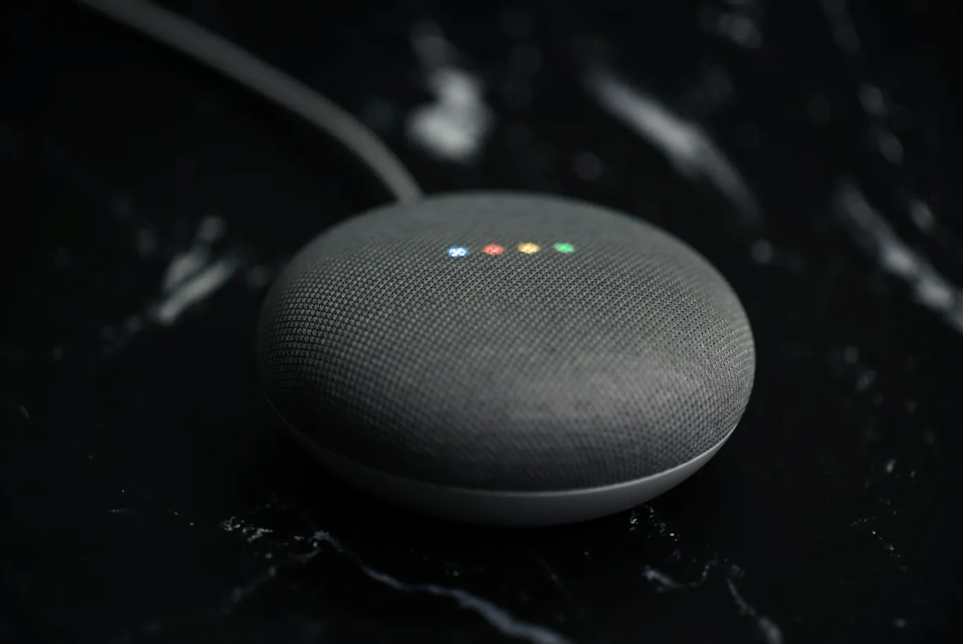 Charcoal fabric smart speaker with glowing indicator lights on a black marble surface