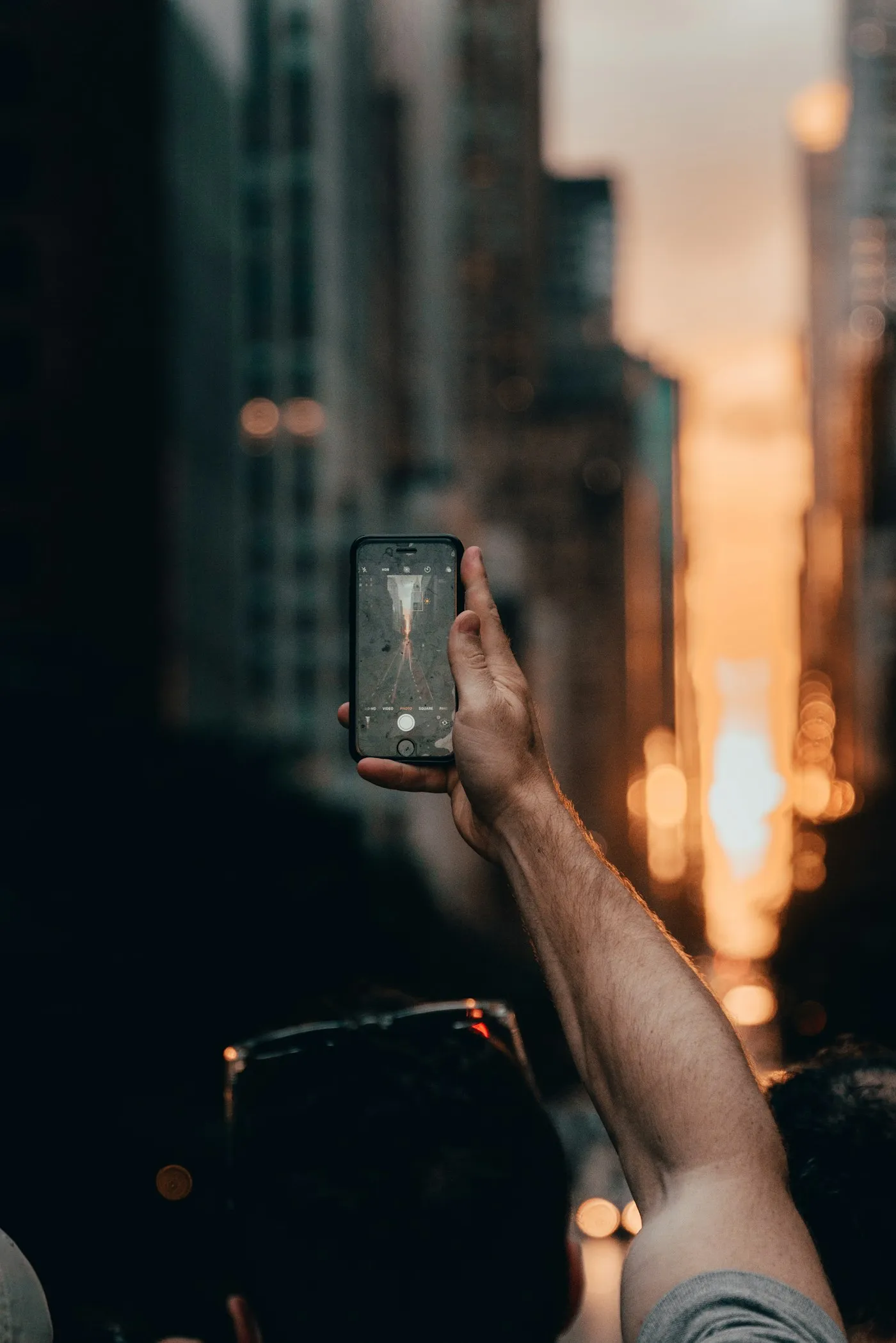 Hand holding up a smartphone to take a photo of glowing city lights at night