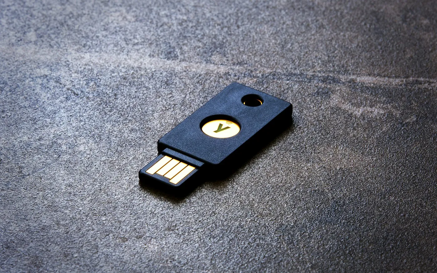 Black USB-A hardware security key with a gold touch button on a dark stone surface