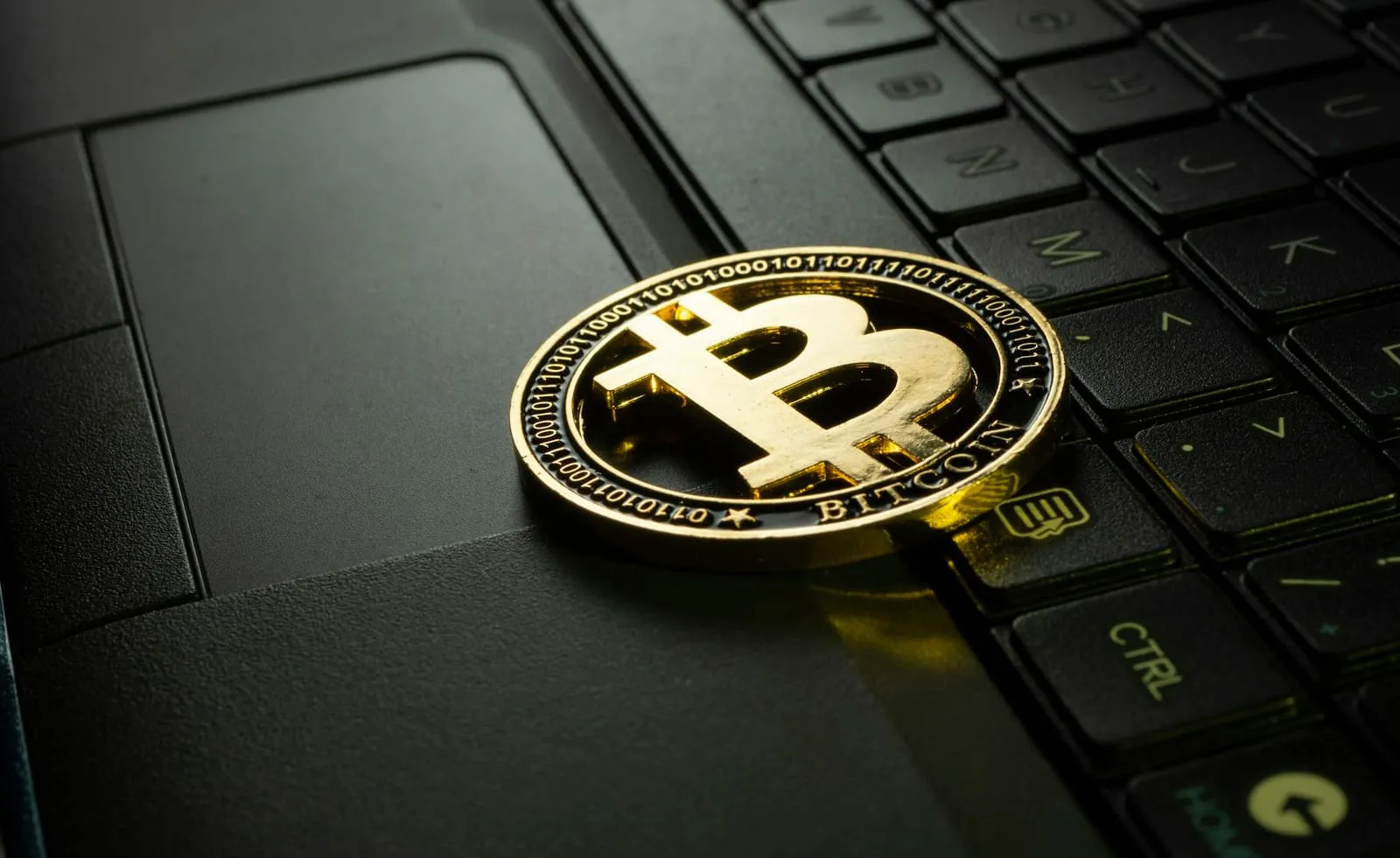 A gold-colored bitcoin coin resting on the keys of a black laptop keyboard