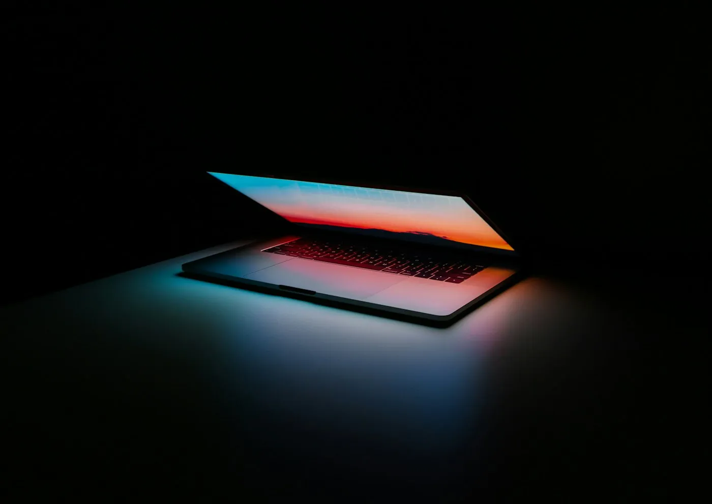 Half-open laptop glowing with blue and orange screen light on a dark desk